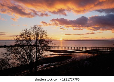 Spectacular Sunset Over White Rock's Silhouetted Pier And Beach.   Colorful Clouds Overhead Are Reflected In Shallow Tide Pools.