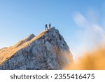 Spectacular view of two hikers walking along the mountain ridge route with the sun on the clear blue sky, aerial shot. Inspiration, nature, and mountaineering concepts.