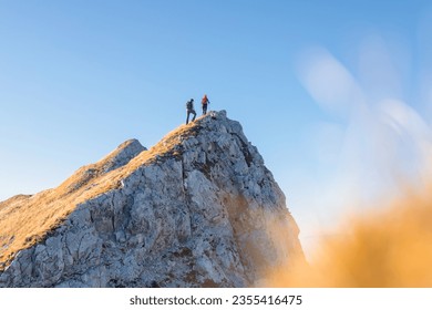 Spectacular view of two hikers walking along the mountain ridge route with the sun on the clear blue sky, aerial shot. Inspiration, nature, and mountaineering concepts. - Powered by Shutterstock