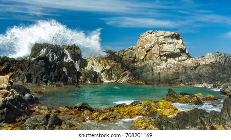 Spectacular wave splashes against the rocks shielding the natural pool (Conchi), a popular tourist attraction, in Aruba.