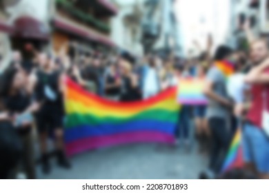 A Spectator Waves A Gay Rainbow Flag At An LGBT Gay Pride March. Blurred Background Concept.