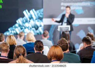 Spectators Listening To Speaker And Watching Presentation On Large Screen During Business Conference In Modern Hall