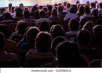 Spectators At A Theater Performance, In A Cinema Or At A Concert. Shooting From Behind. The Audience In The Hall. Silhouettes Of People.