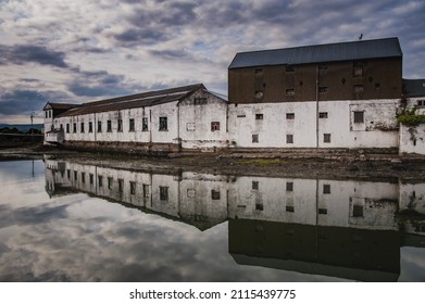 Spectral Vartry River in Wicklow town industrial port with the old harbour buildings reflecting on the still, flat water. Eerie forsaken harbor buildings in a silent ghostly fishermen village. Ireland