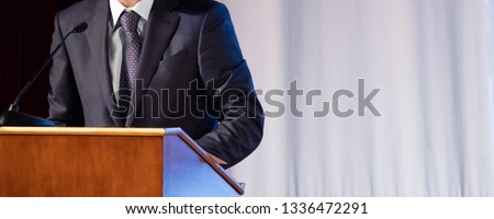 Speech of an abstract man in a suit on stage at the stand for performances. Tribune or pulpit for speaker official, president or professor. Close-up. Copy space.
