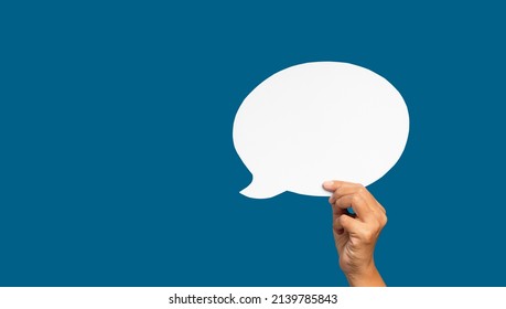 A speech bubble concept. Hand holding of an empty white speech bubble against a blue background. Space for text. Close-up photo. - Shutterstock ID 2139785843