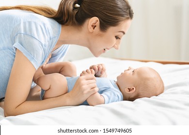 Speech and language development for babies. Young mother playing with her cute newborn baby in bed, side view