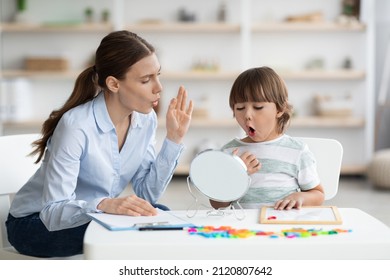Speech therapy concept. Cute little boy pronouncing sound O looking at mirror, professional woman therapist teaching kid right pronounciation during private lessong at office - Shutterstock ID 2120807642