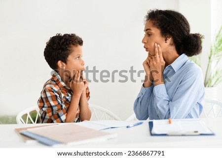 Speech Therapy Session. Woman working on kid boy pronunciation sitting at desk indoors. Professional speech therapist lady helping little patient with stuttering issue. Logopedic correction