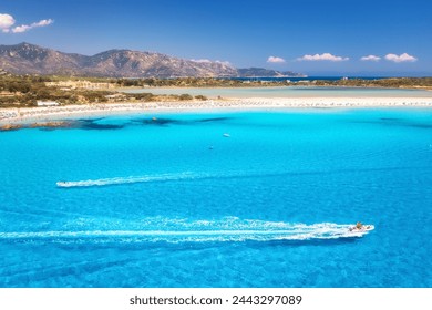 Speed boat in transparent blue water and white sandy beach at sunny day in summer. Travel in Sardinia, Italy. Top view from drone of sea coast, motorboats, mountain, trees, sky. Tropical. Aerial view