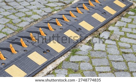 Speed bump featuring orange reflective markers on a cobblestone street with grass