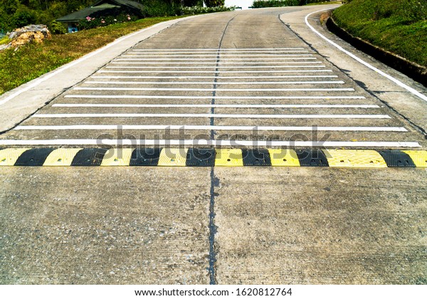 Speed bump road and rumble strip road background.\
Black and yellow speed bump line road and white rumble strip lines\
on concrete road surface