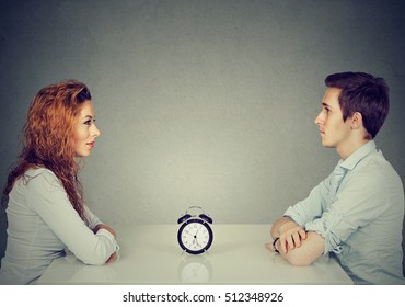 Speed dating. Man and woman sitting across from each other at table with alarm clock in-between  