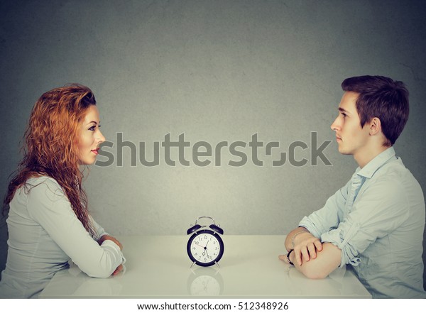 Speed dating. Man and woman\
sitting across from each other at table with alarm clock in-between\
 