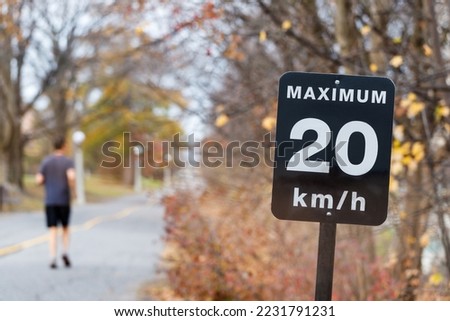Speed limit sign, 20 kilometers per hour for bicycle lanes. Man jogging in park.
