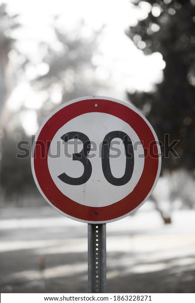 Speed limit sign in the country side\
on a summer evening. The speed limit is 30 kmh on a gravel road.\
The focus point is on the speed limit sign on the\
right.