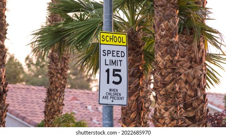 A speed limit sign indicating maximum speed of 15 M.P.H. (miles per hour) in a school zone. Effective when children are present during school days. Captured in Las Vegas, NV, USA in early morning.