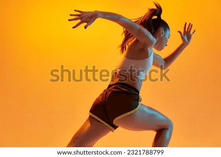 Speed, strength. Young girl, professional athlete, runner in motion, training over orange studio background in neon light. Concept of sportive lifestyle, health, endurance, action and motion. Ad