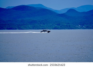 A speedboat cruising on a tranquil lake with lush green mountains in the background under a clear blue sky. - Powered by Shutterstock