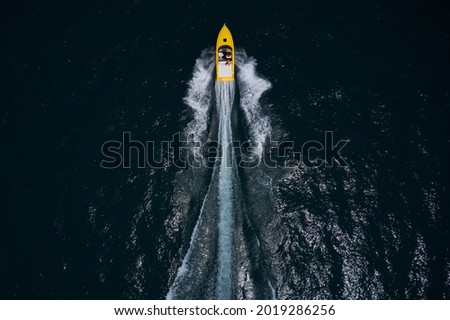 Speedboat on dark blue water aerial view. Large yellow boat moving on dark water. Speedboat wave speed water. Speed boat faster movement on the water top view. 