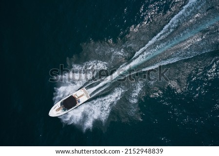 Speedboat on dark water aerial view. Boat trip at sea. White boat with a black awning movement on the water drone view.