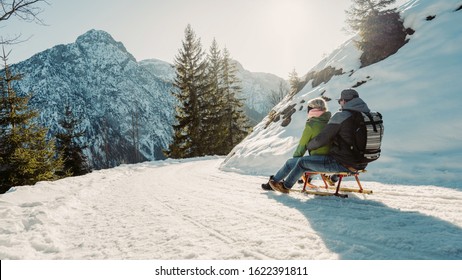 Speeding Downhill On Wooden Sled. Happy Influencers Couple Having Fun With Wood Vintage Sledding On Snow High Mountains - Young Crazy People Enoying Winter Vacation - Travel And Holiday Concept