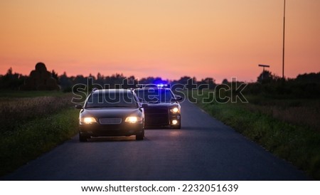 Speeding Driver Gets Pulled Over By Police Patrolling Car . Wide Shot of the Two Cars Stopped in a Road Crossing an Open Field. Drunk Driver Gets Caught by Professional Officers