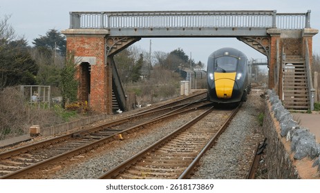 A speeding inter city express train passing under an old brick and metal footbridge near Dawlish Warren in Devon UK
