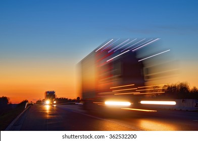 Speeding motion blur oncoming trucks with glowing lights on the highway after sunset. Shining the spotlight cars. Blue and orange bright sky at dusk.