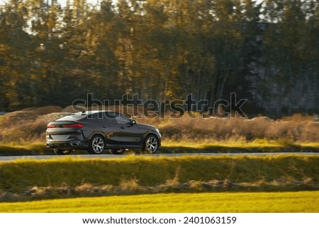Speeding on a road in a sporty luxury car with a sunset and forest background. Sophisticated expensive car on the road. Premium and Elegant luxurious car on the highway.