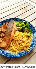 Speghetti Agolio Olio With Pan Fried Salmon, Stir Fried Broccoli And Mushrooms. Done By Private Chef. Food Placed On Wooden Table At Sun Deck 