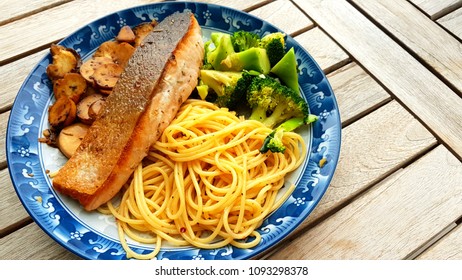 Speghetti Agolio Olio With Pan Fried Salmon, Stir Fried Broccoli And Mushrooms. Done By Private Chef. Food Placed On Wooden Table At Sun Deck 