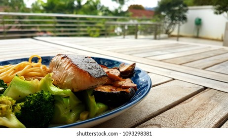 Speghetti Agolio Olio With Pan Fried Salmon, Stir Fried Broccoli And Mushrooms. Done By Private Chef. Food Placed On Wooden Table At Sun Deck 