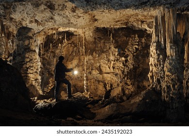 A speleologist with a carbide lamp poses in a cave dome with rich stalactite and stalagmite decorations.