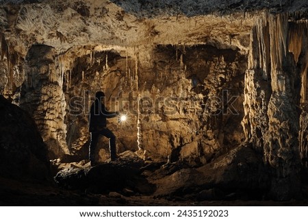 A speleologist with a carbide lamp poses in a cave dome with rich stalactite and stalagmite decorations.