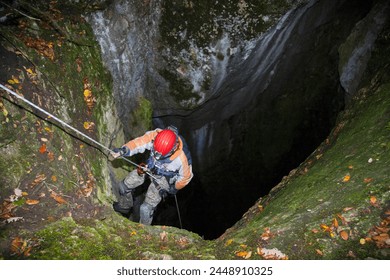 A speleologist man exploring a huge hidden cave hanging on a rope for safety and preparing to go down into the cave - Powered by Shutterstock