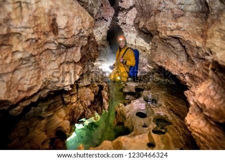 Speleologist in red helmet with light stands in the water in the cave gallery with curve walls and caverns. Karst cave Leningradskaya. Caucasian mountains. 