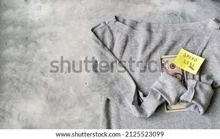 SPEND LESS. gray cotton T-shirt on a gray background with dollars and a sticker with the inscription 