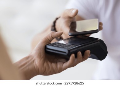 Spend money by electronic mobile banking application, convenient, instant cashless payment. Unknown male hand holding smart phone paying bills using portable payment terminal machine, close up view
