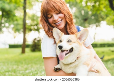 Spending free time with pet together. Happy young caucasian young woman teenage girl walking having fun taking care of her pet dog welsh corgi outdoors in park, forest, garden.