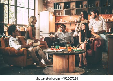 Spending great time with best friends. Group of cheerful young people enjoying food and drinks while spending nice time in cofortable chairs on the kitchen together