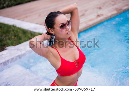 Spending hot summer day poolside. Beautiful young woman in red bikini relaxing by the pool.
