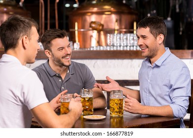 Spending Time In Bar. Three Cheerful Friends Drinking Beer In Bar 