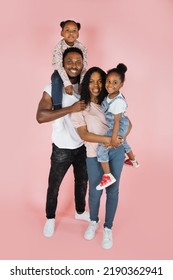 Spending time with family is fun. Full body length of excited african american man, woman and girls laughing and posing isolated on pink studio wall. Cheerful father carrying daughter on back