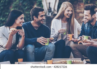 Spending Time With Friends. Group Of Cheerful Young People Talking To Each Other And Eating Pizza While Sitting Outdoors