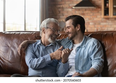 Spending Time With Parent. Happy Two Diverse Age Men Generations Retired Dad Young Son Sit On Sofa Hug Talk Speak Chat Meeting At Home On Weekend. Smiling Old Father Share Plans Ideas With Adult Child