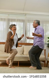 Spending time together at home, an elderly Asian couple having fun dancing in the living room.