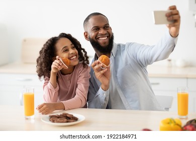 Spending Time Together. Portrait Of Happy African American Family Taking Selfie While Eating In The Kitchen At Home, Using Mobile Phone. Smiling Black Dad And Daughter Making Photo, Having Breakfast