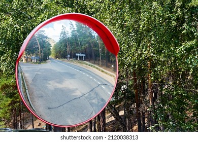 Spherical Road Mirror At The Intersection Of Roads In The Forest Against The Background Of Green Trees