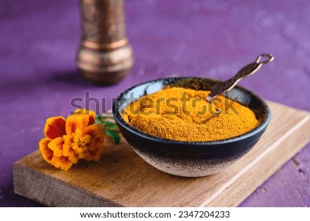 Spice, Imereti saffron or dried ground marigold flowers in a brown clay bowl on a purple concrete background. Spices of the world. Georgian spices